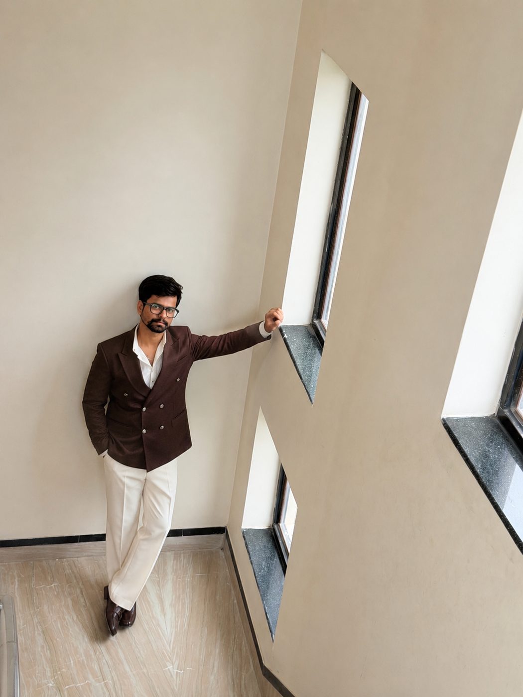 Sharad Nandwana in a brown double-breasted blazer against warm stairwell light